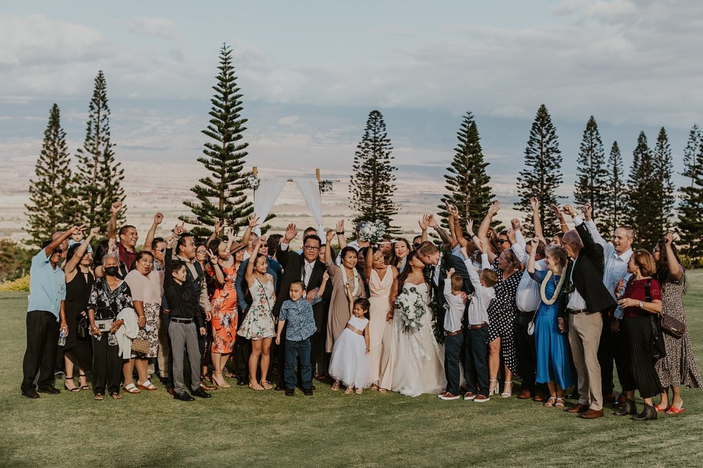Bride and Groom kissing with guests raising their hands in celebration portrait