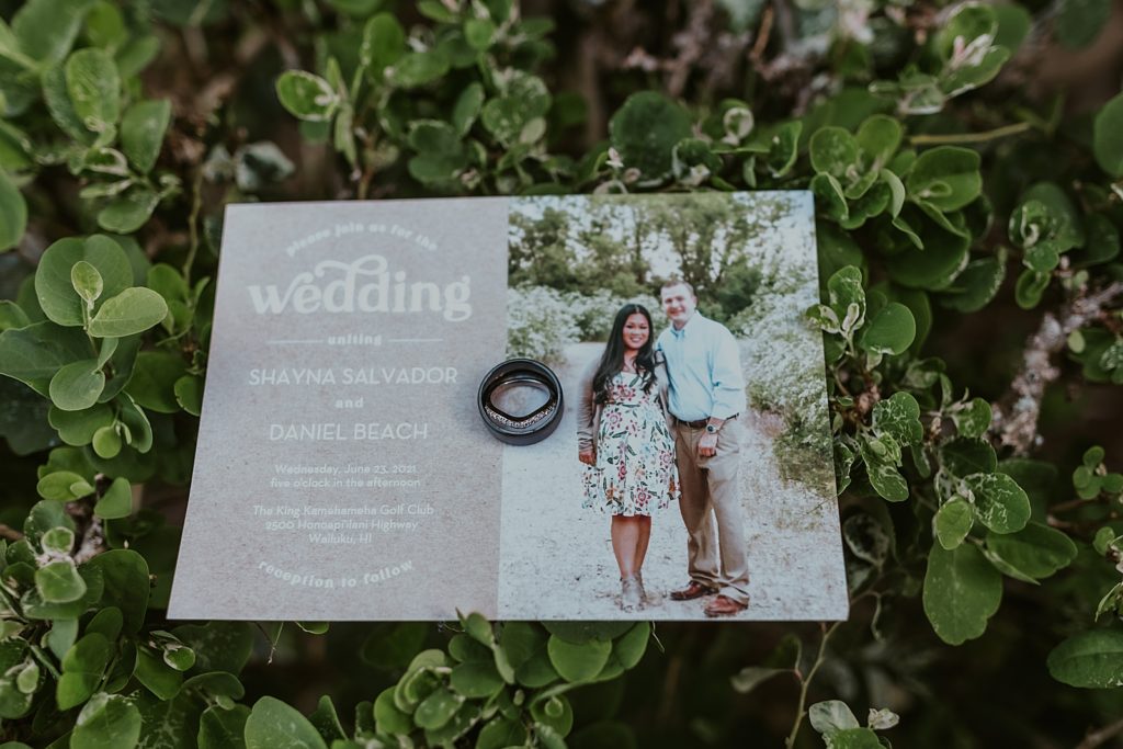 Detail shot of wedding bands on invitation on green bush
