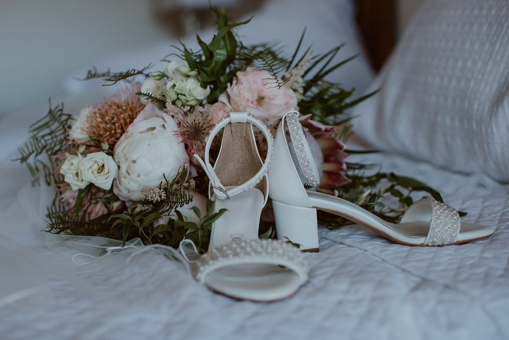 Detail shot of white pearl heels by bouquet
