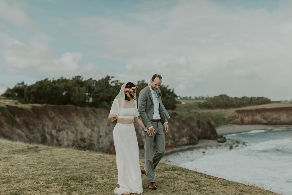 Bride and Groom holding hands walking by green cliffs