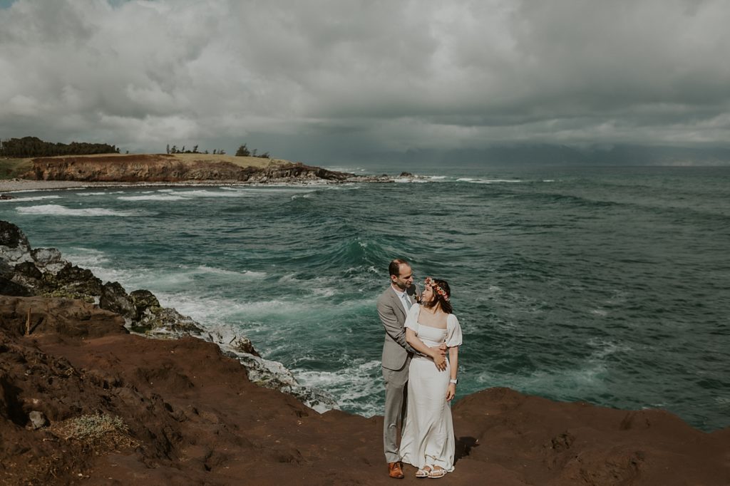 Groom holding Bride in front of ocean shoreline