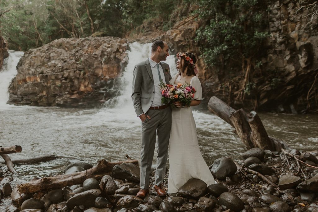 Bride and Groom looking at each other in front of forest waterfall