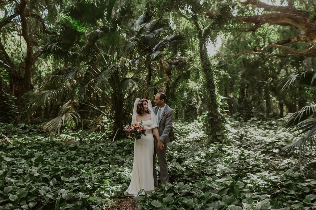 Bride and Groom holding hands and looking at each other in tropical greenery forest