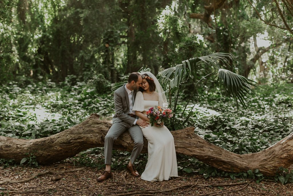 Bride and Groom sitting on fallen tree trunk in green forest