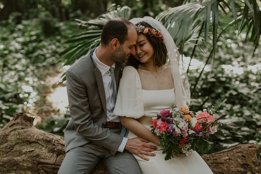 Closeup of Bride and Groom sitting on tree trunk and nuzzling their heads