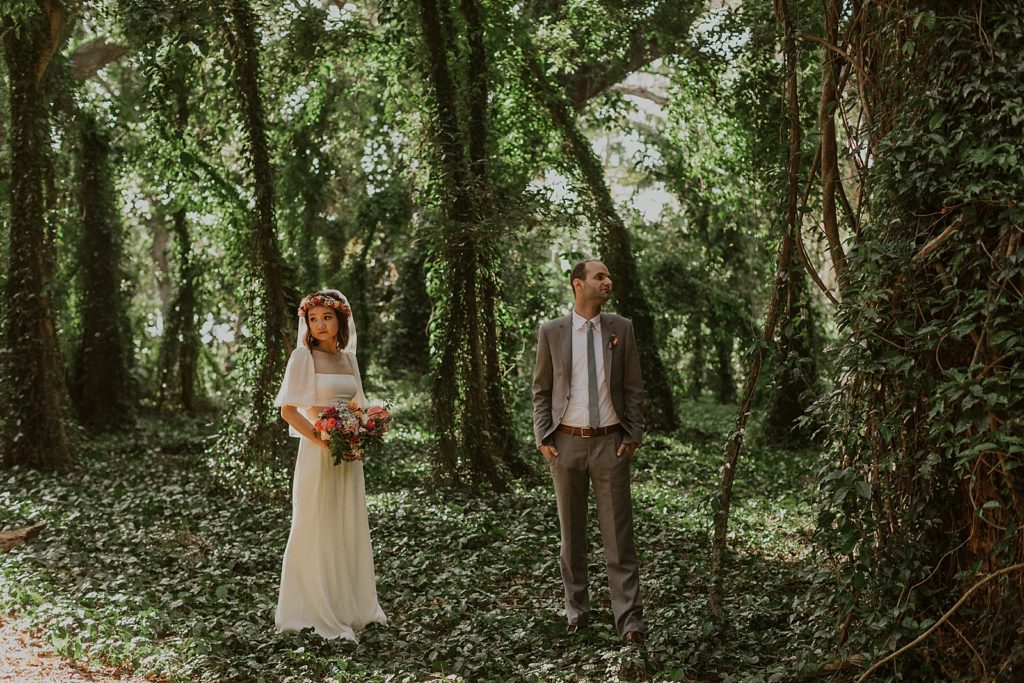 Bride and Groom standing in green forest looking at green vine trees