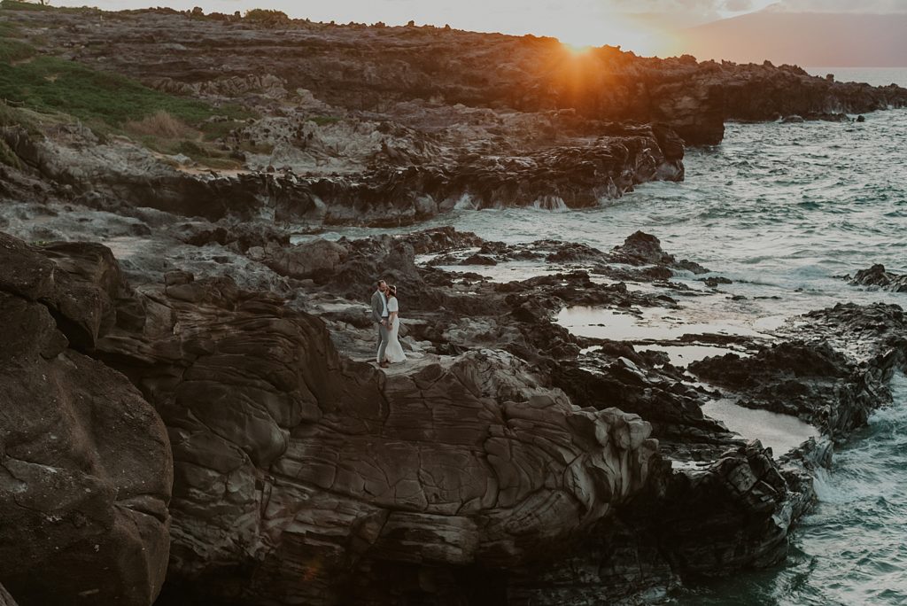 Wide shot of Bride and Groom on rocky cliff by the ocean