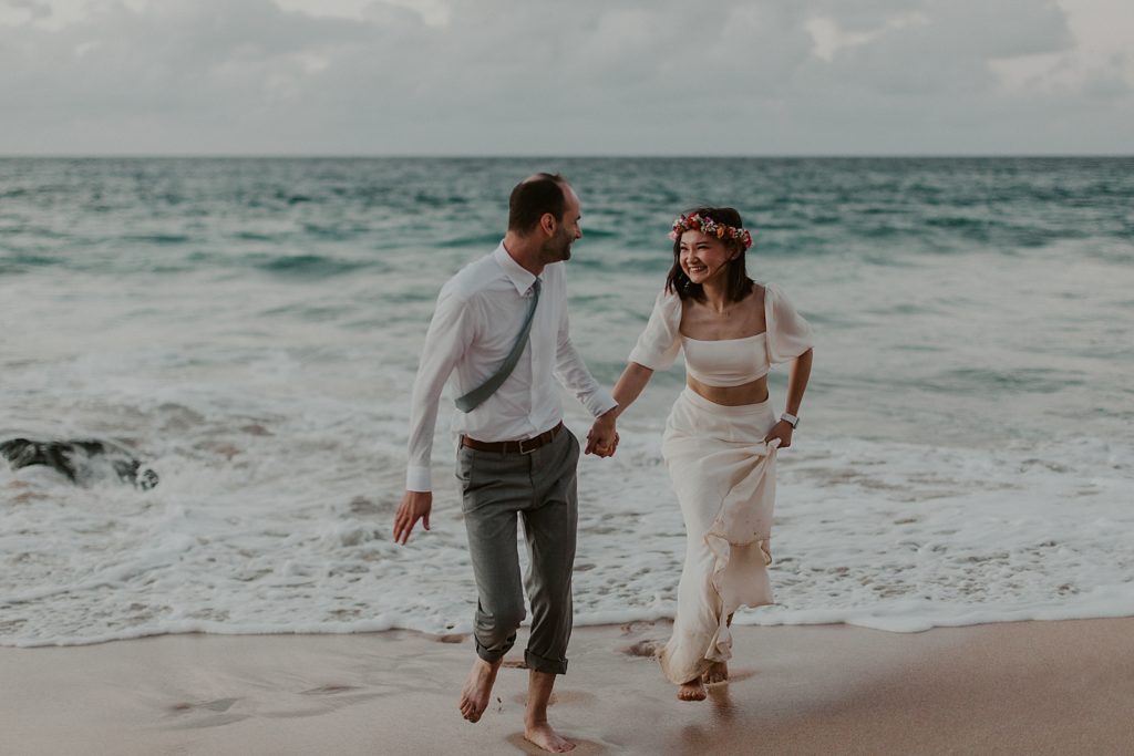 Bride and Groom holding hands and running from ocean water coming in