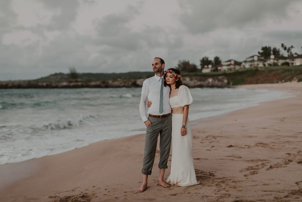 Bride and Groom holding each other on the sand by the ocean shoreline