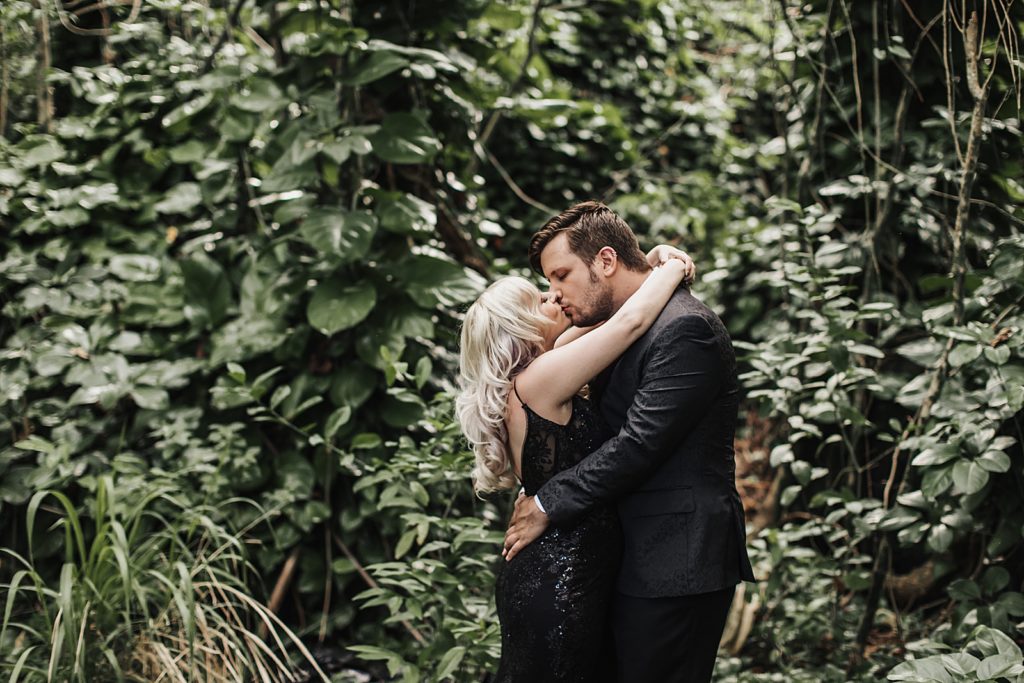 Bride and Groom both in black kissing around the greenery