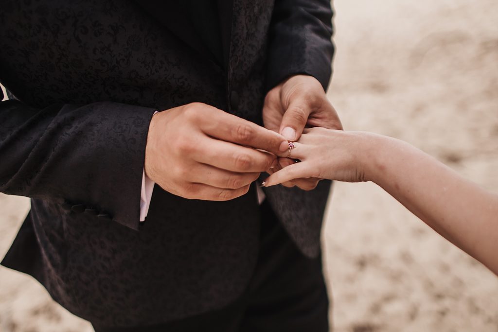 Closeup of Groom putting ring on Bride's finger on the sand