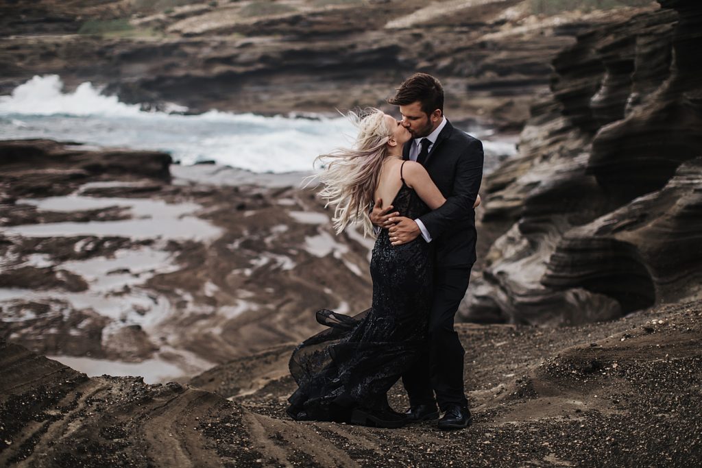 Bride and Groom holding each other and kissing on volcanic sand