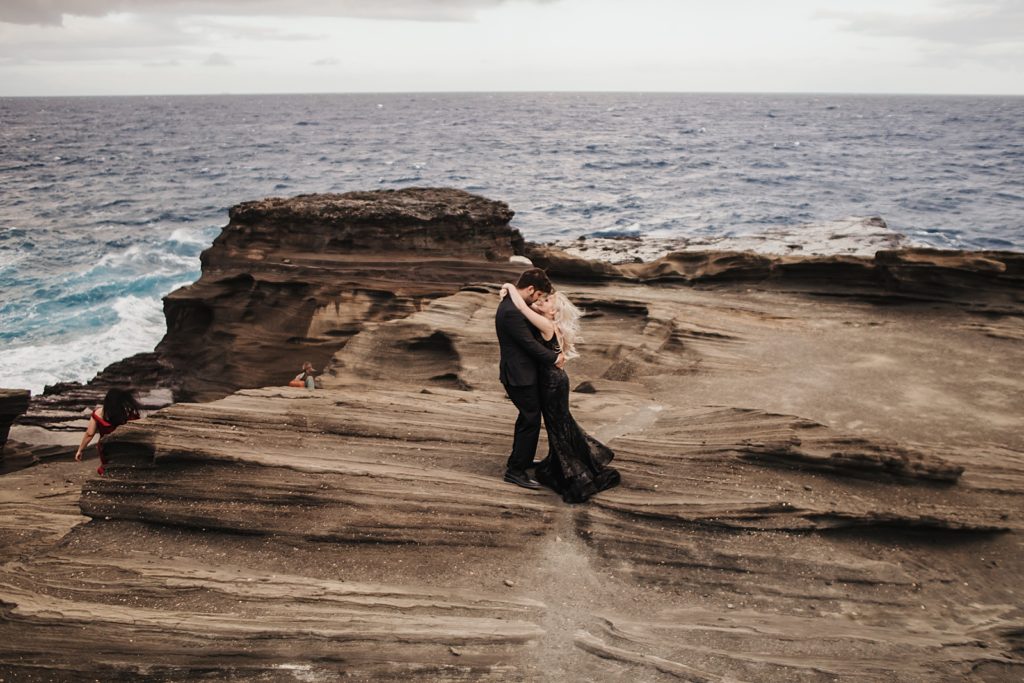 Bride and Groom holding each other on ocean side smooth rock