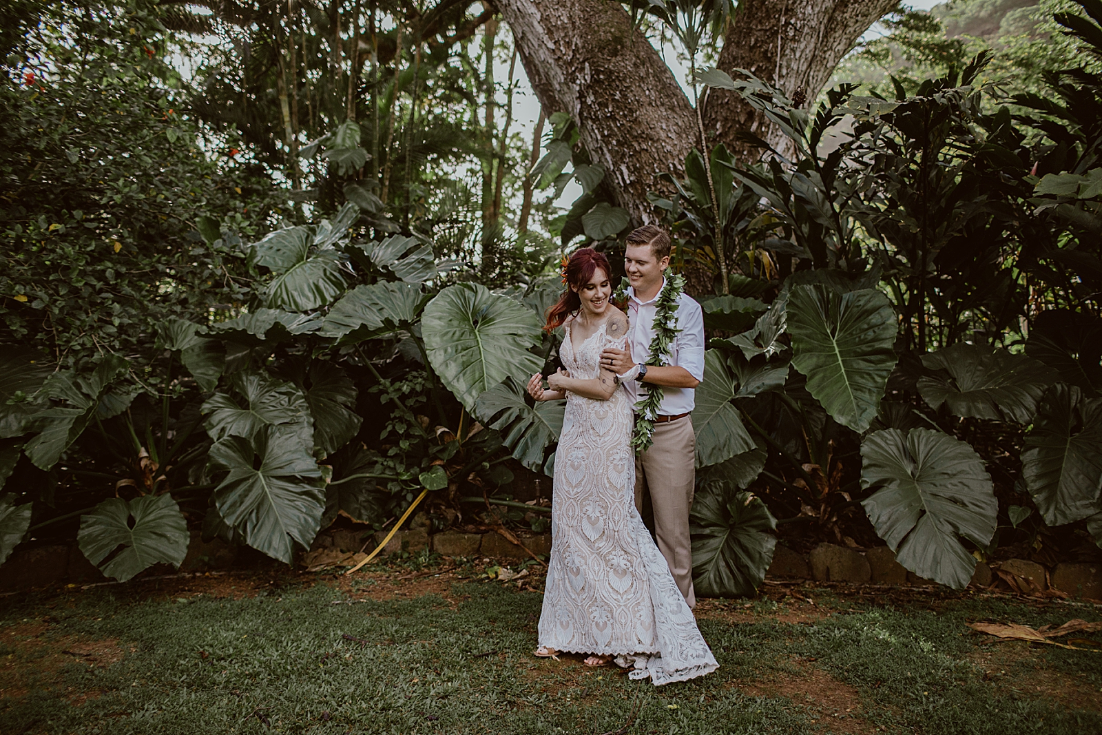 Groom holding Bride in front of tropical green plants