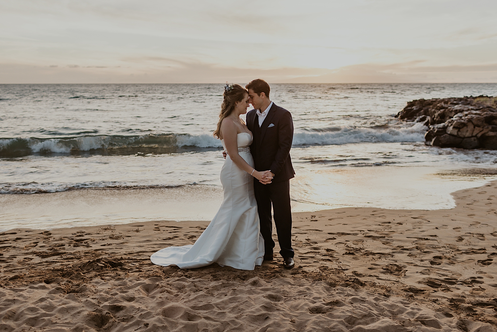 Bride and Groom nuzzling on the sand by incoming ocean waves