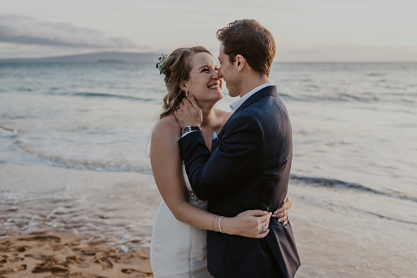 Bride and Groom holding each other and nuzzling their noses by the ocean