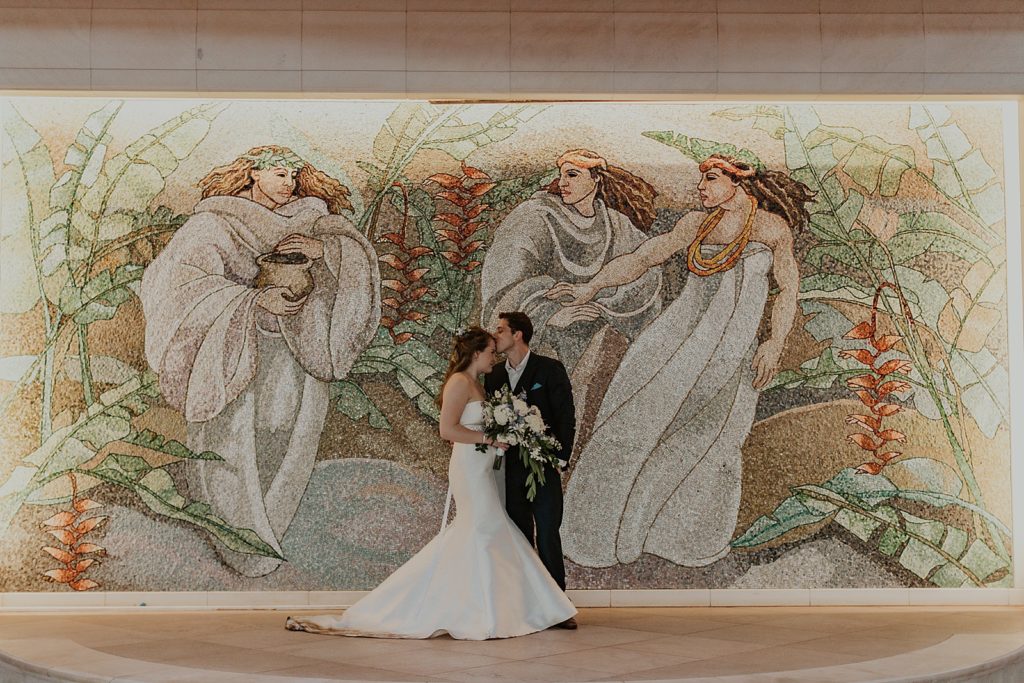 Groom kissing Bride's forehead in front of mural