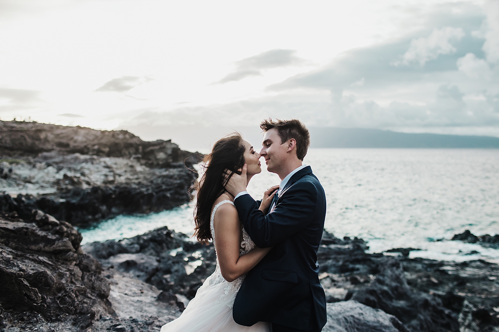 Bride and Groom kissing on rocky terrain next to ocean