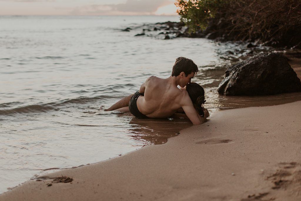 Couple laying in sand together and cuddling while ocean waves come in gently