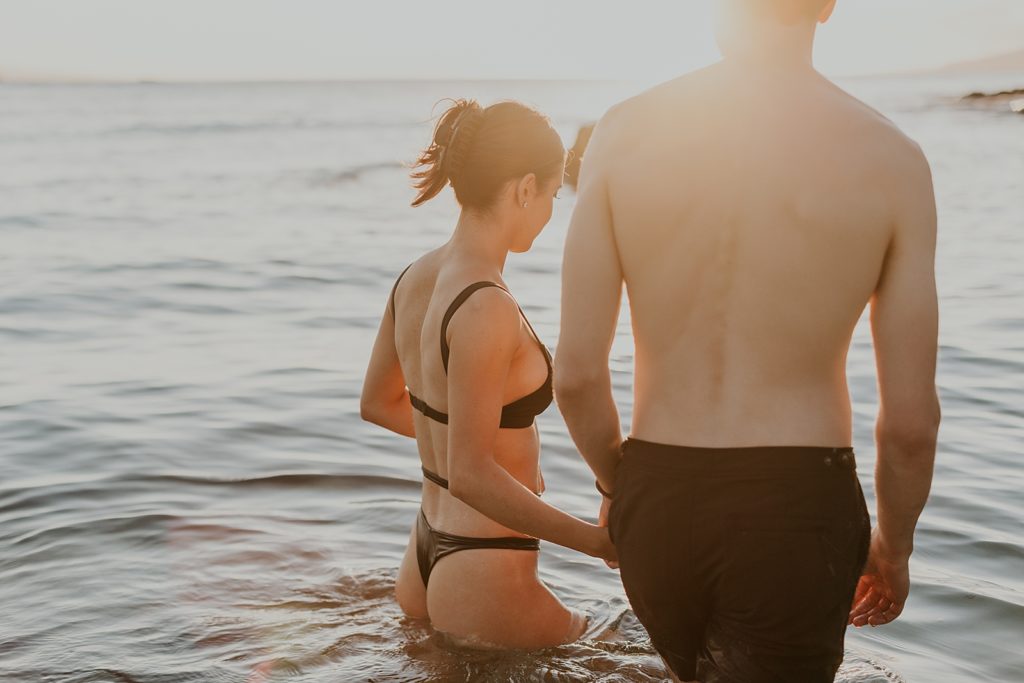 Candid shot of couple walking in the ocean with the sunrays coming through