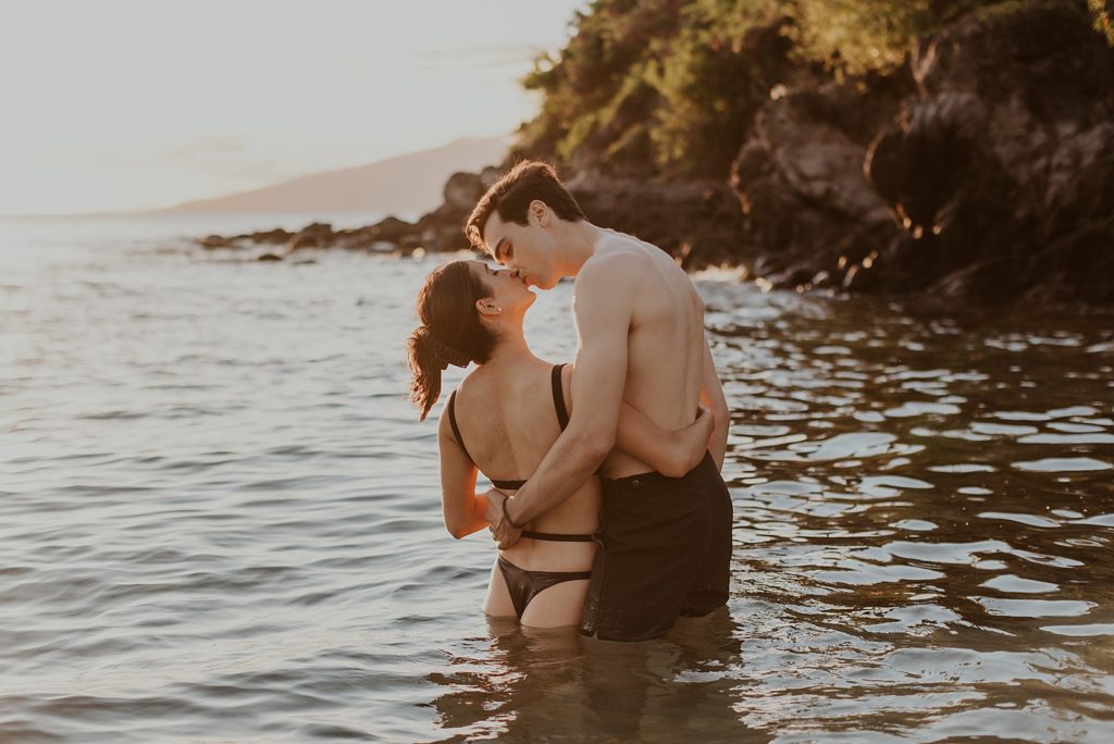 Couple kissing while knee deep in ocean water by cliff