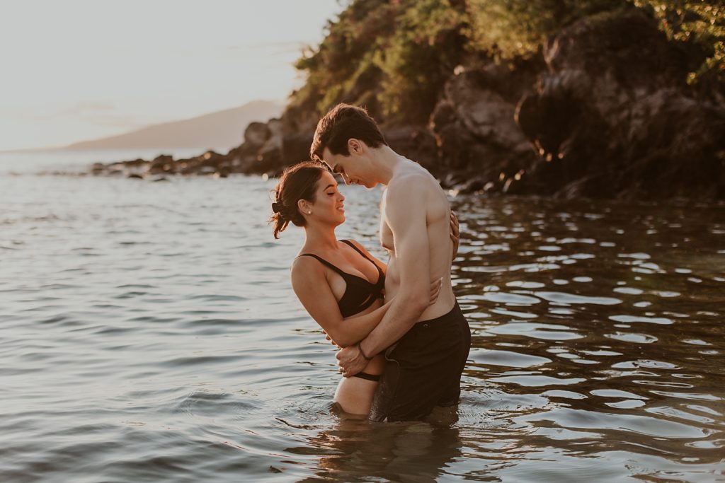 Couple holding each other close while standing in shallow ocean water looking at each other