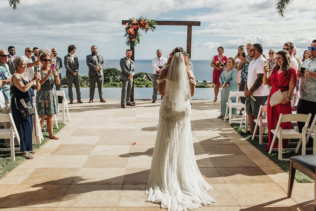 Wide shot of Bride entering outdoor Ceremony with guests standing and Groom watching