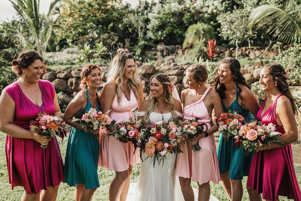 Bride with Bridesmaids in different colored dresses and holding bright bouquets outside