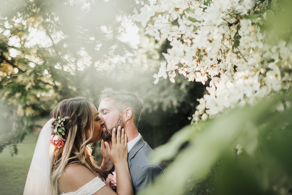 Bride and Groom kissing by branches with flowers 