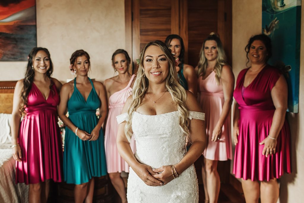 Bridesmaids in different color dresses looking at Bride ready in wedding dress