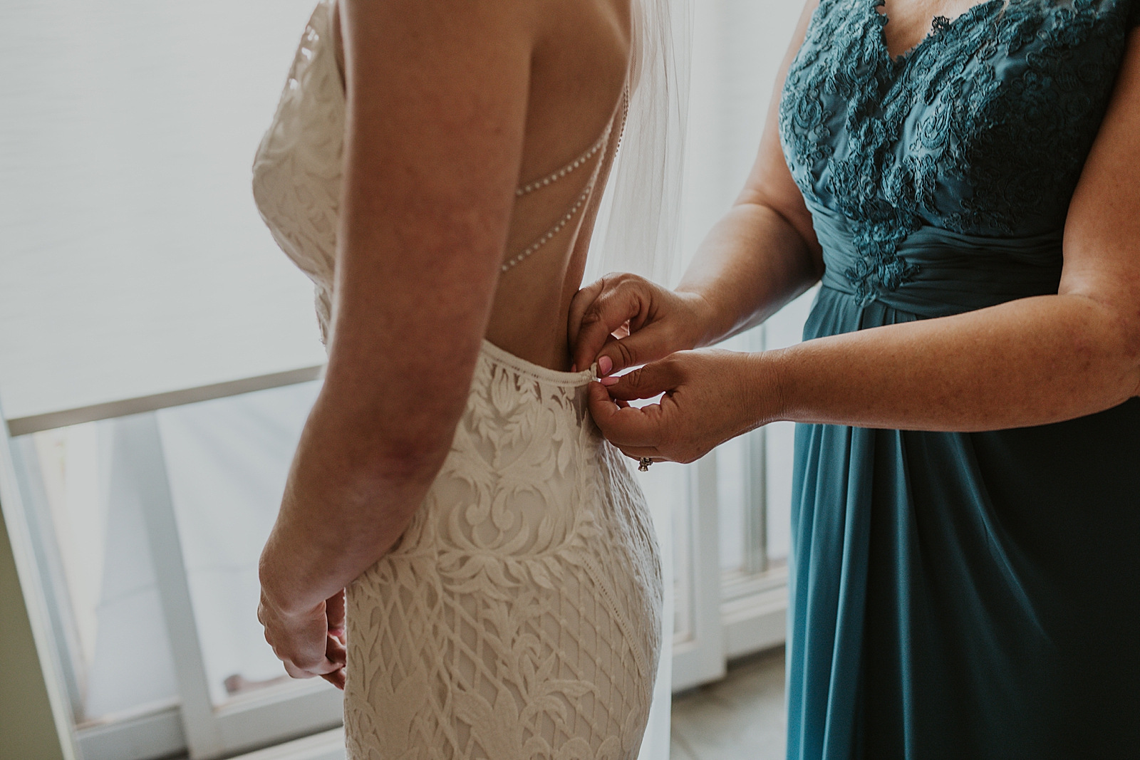 Mother helping Bride get wedding dress buttoned by the window