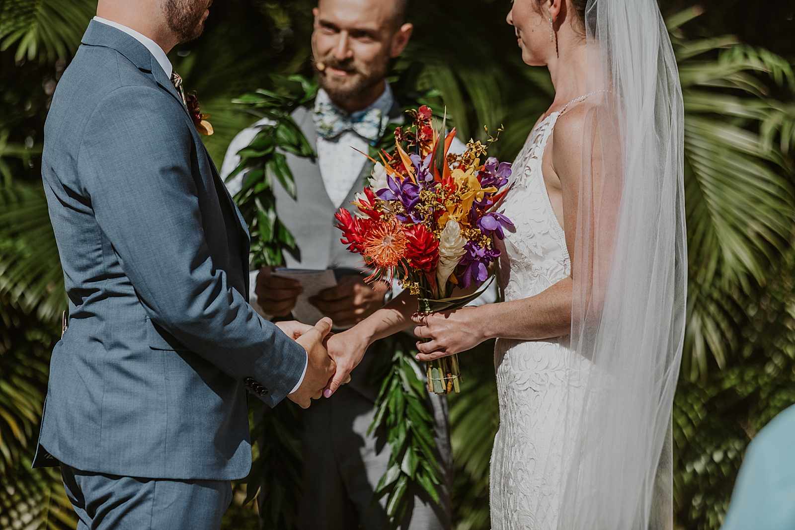 Closeup of Bride and Groom holding hands with Bride holding tropical bouquet