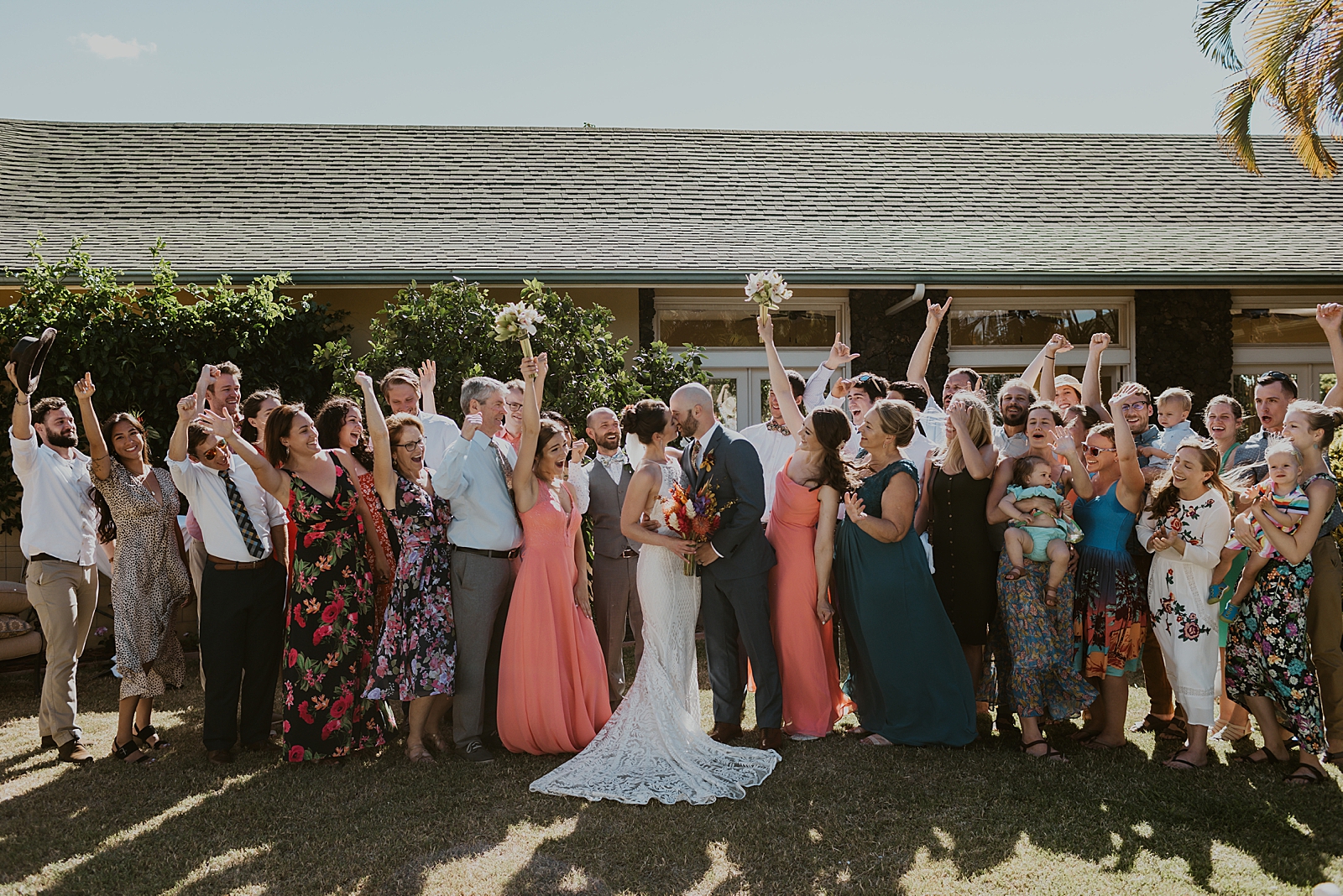 Bride and Groom kissing with family and friends raising hands celebrating by house