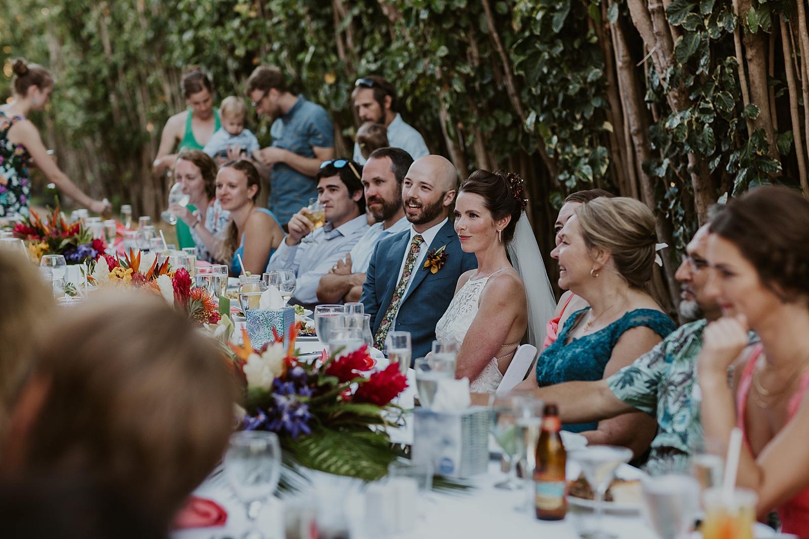 Shot of Bride and Groom sitting with guests at long Reception table