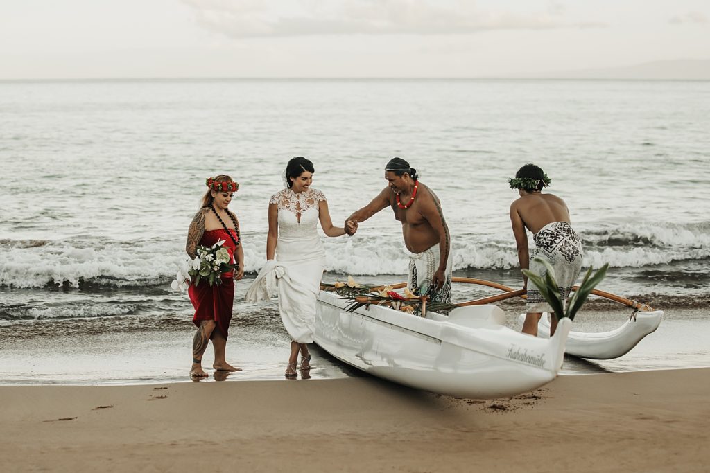 Bride with Bridesmaid coming out of boat on ocean shoreline