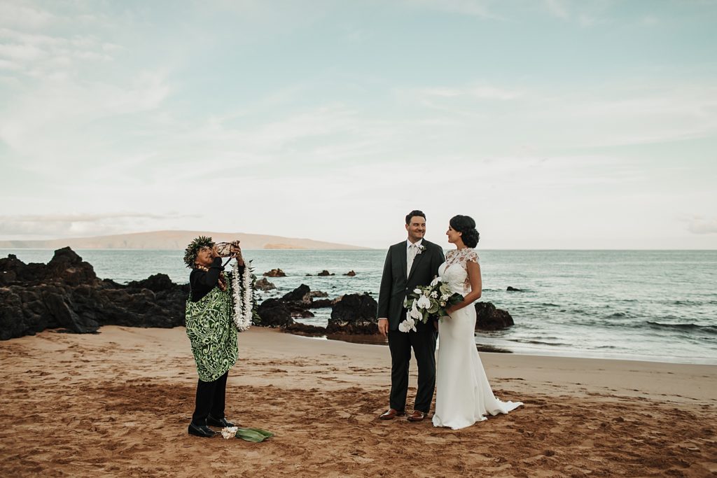 Officiant blowing instrument with Bride and Groom on the sand by the ocean