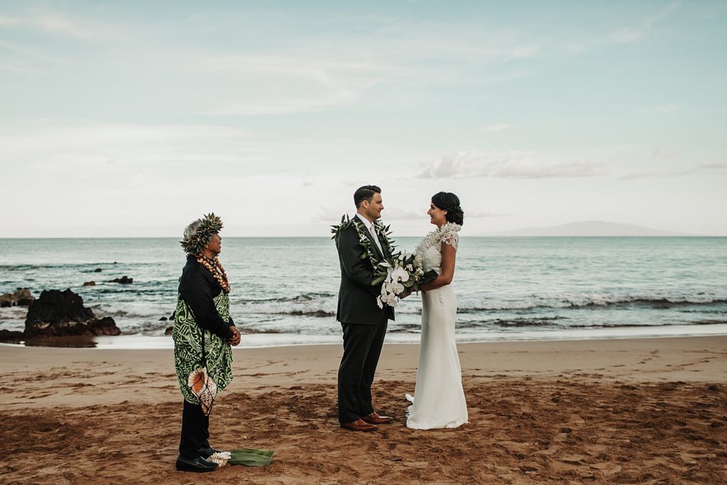 Bride and Groom holding hands and looking at each other with officiant nearby by the ocean