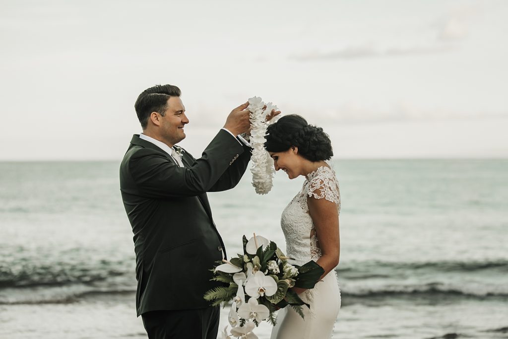 Groom putting floral necklace on Bride by the ocean