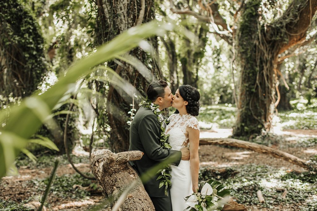 Bride and Groom kissing while leaning on a fallen tree trunk in the forest
