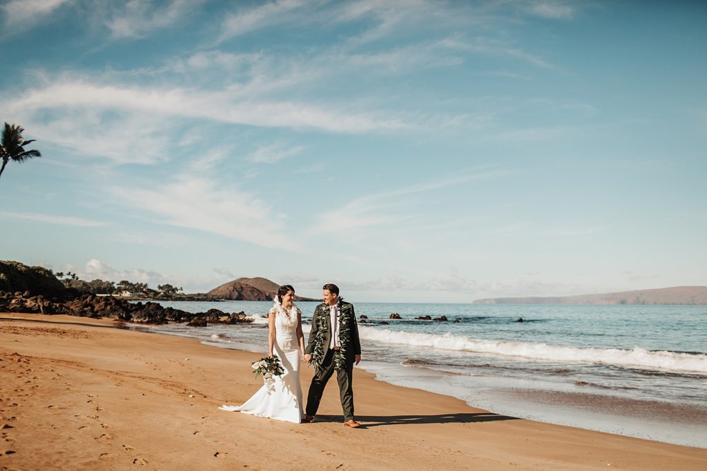 Bride and Groom holding hands and walking on the sand together by the ocean
