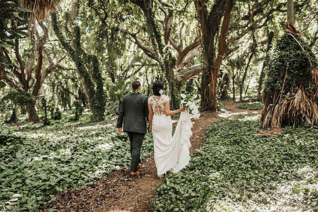 Bride and Groom holding hands and walking on the dirt path by greenery in the forest