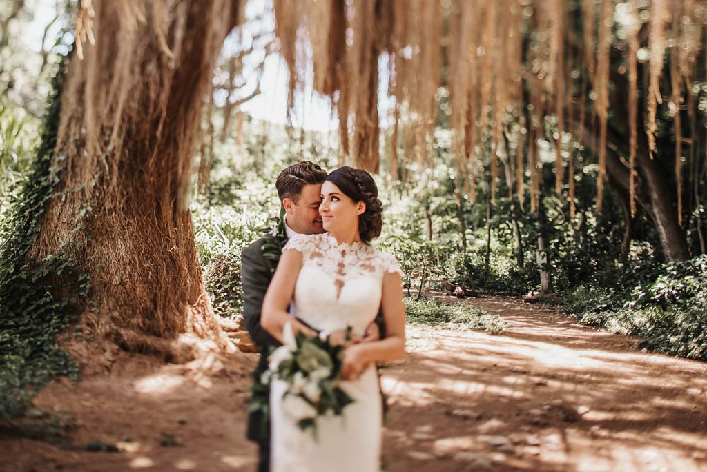 Groom holding Bride from behind and nuzzling his face in the forest