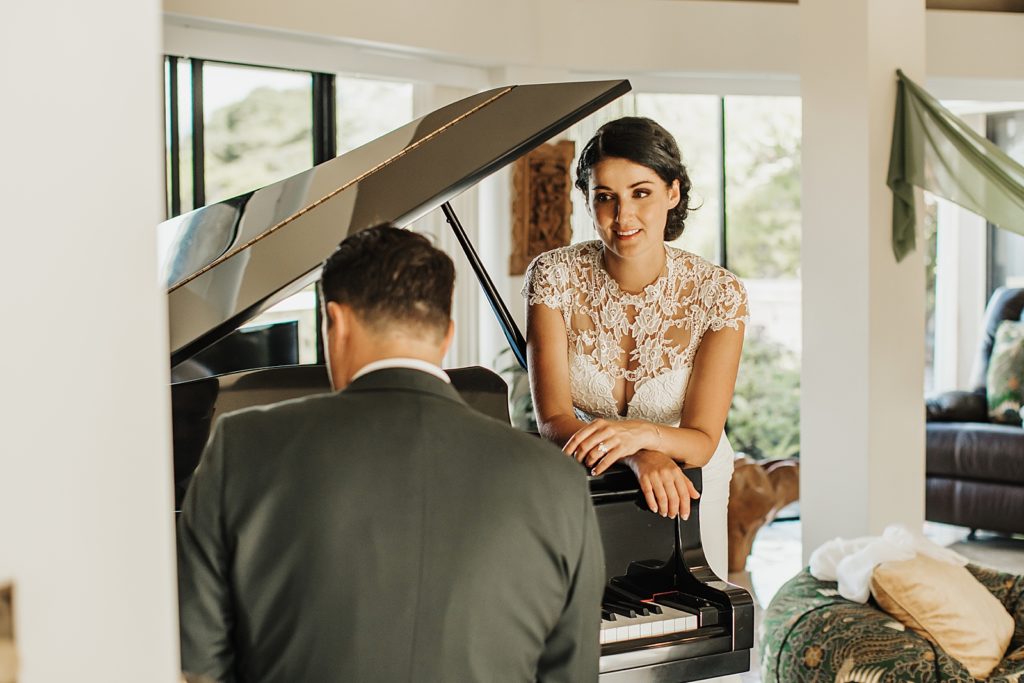 Bride leaning in to listen to Groom play piano inside