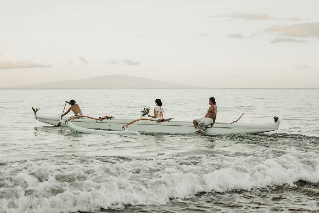 Bride being rowed by paddlers to destination in the ocean