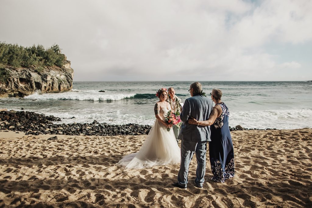 Bride and Groom standing together on the sand with parents watching them