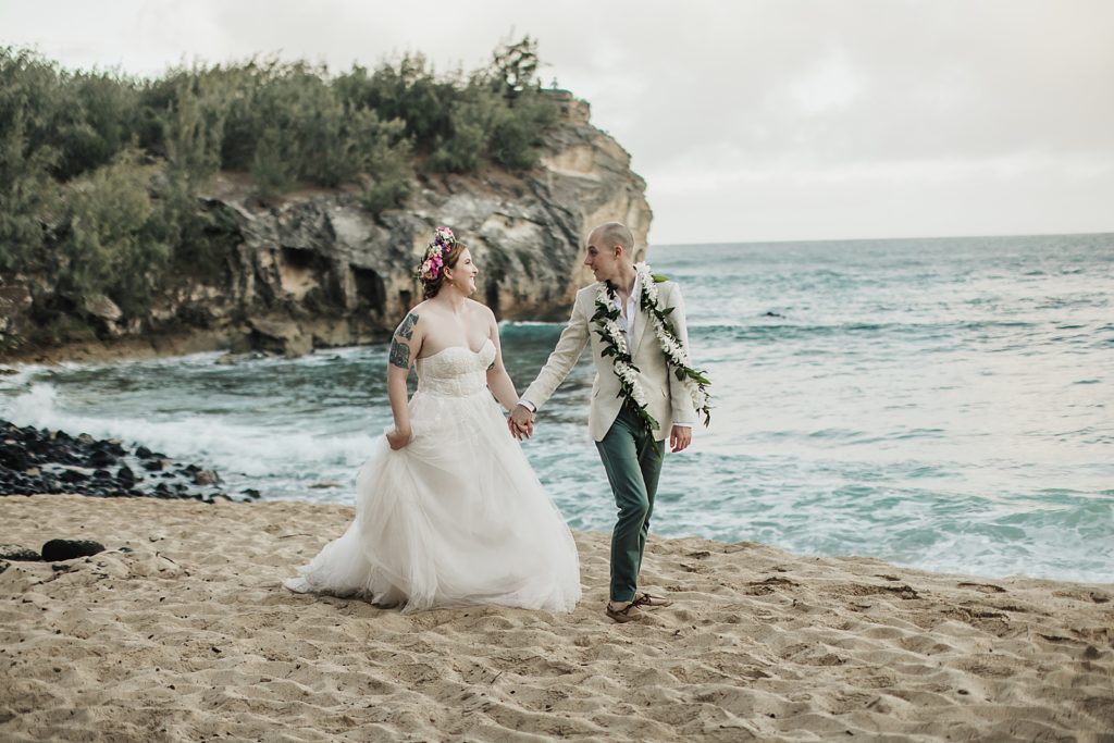 Bride and Groom holding hands walking on the beach together with ocean waves coming in