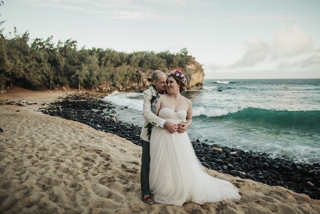 Groom hugging Bride from behind on the beach