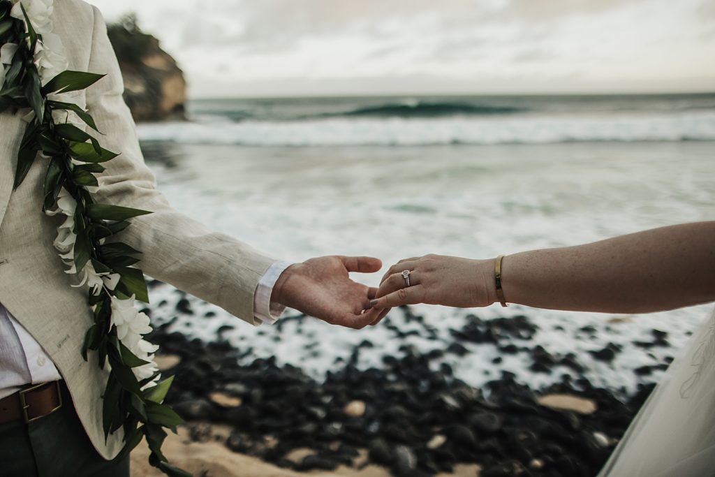 Closeup of Bride and Groom glazing each others hands with the ocean behind them