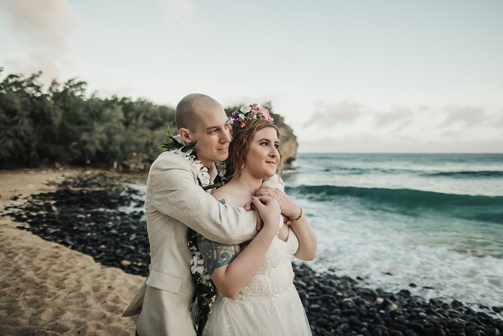 Groom holding Bride from behind and looking at the ocean together