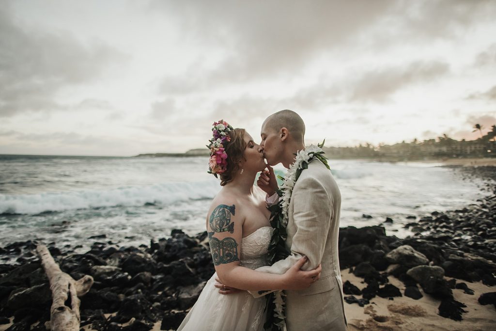 Bride and Groom kissing on the beach with black rocks on the shore